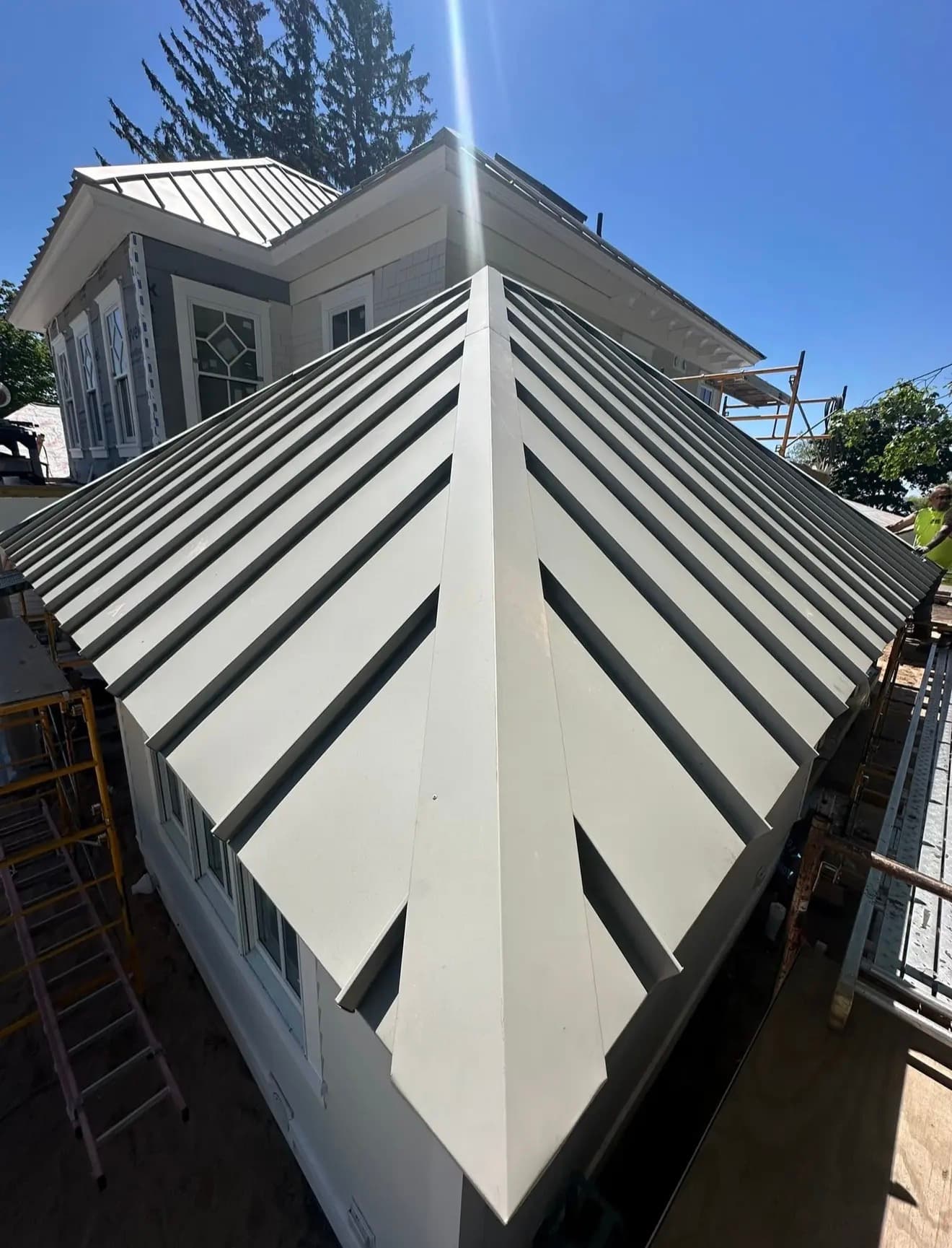 Newly installed standing-seam metal hip roof, sharp diagonal seams converging at the peak
