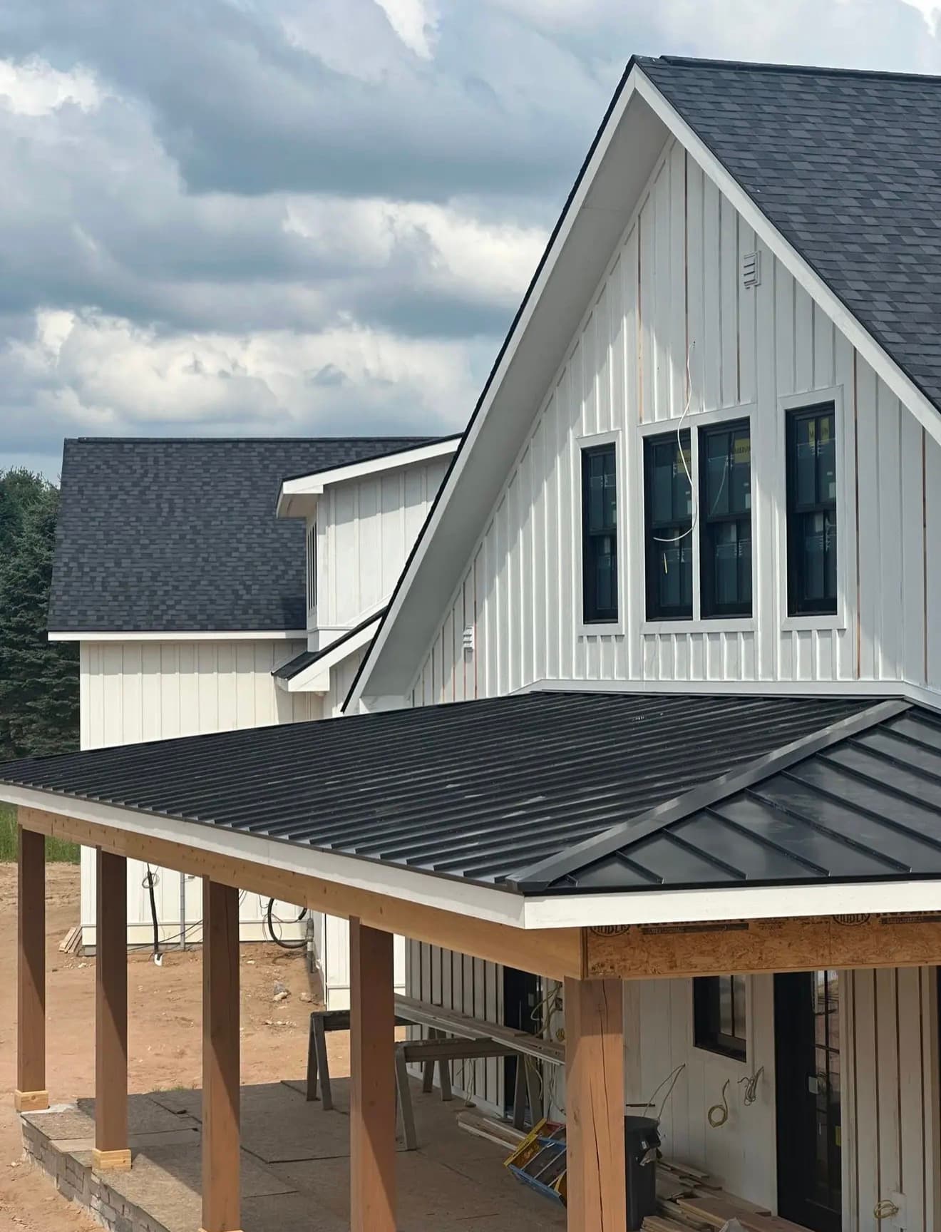 White board-and-batten home with new architectural asphalt shingles and a black standing-seam porch roof beneath dramatic clouds