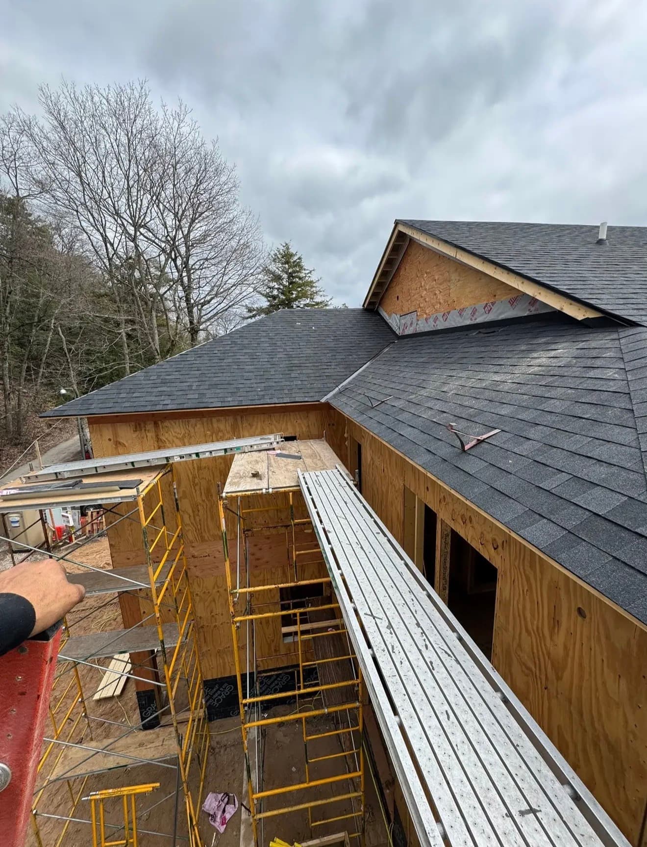 Crew on a partially-shingled Northern Michigan home with scaffolding and dormers visible against grey sky