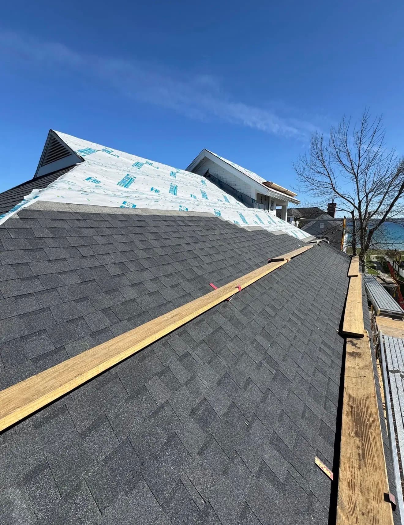 Looking up the slope of a freshly installed architectural asphalt roof toward the peak, house wrap visible above the shingle line